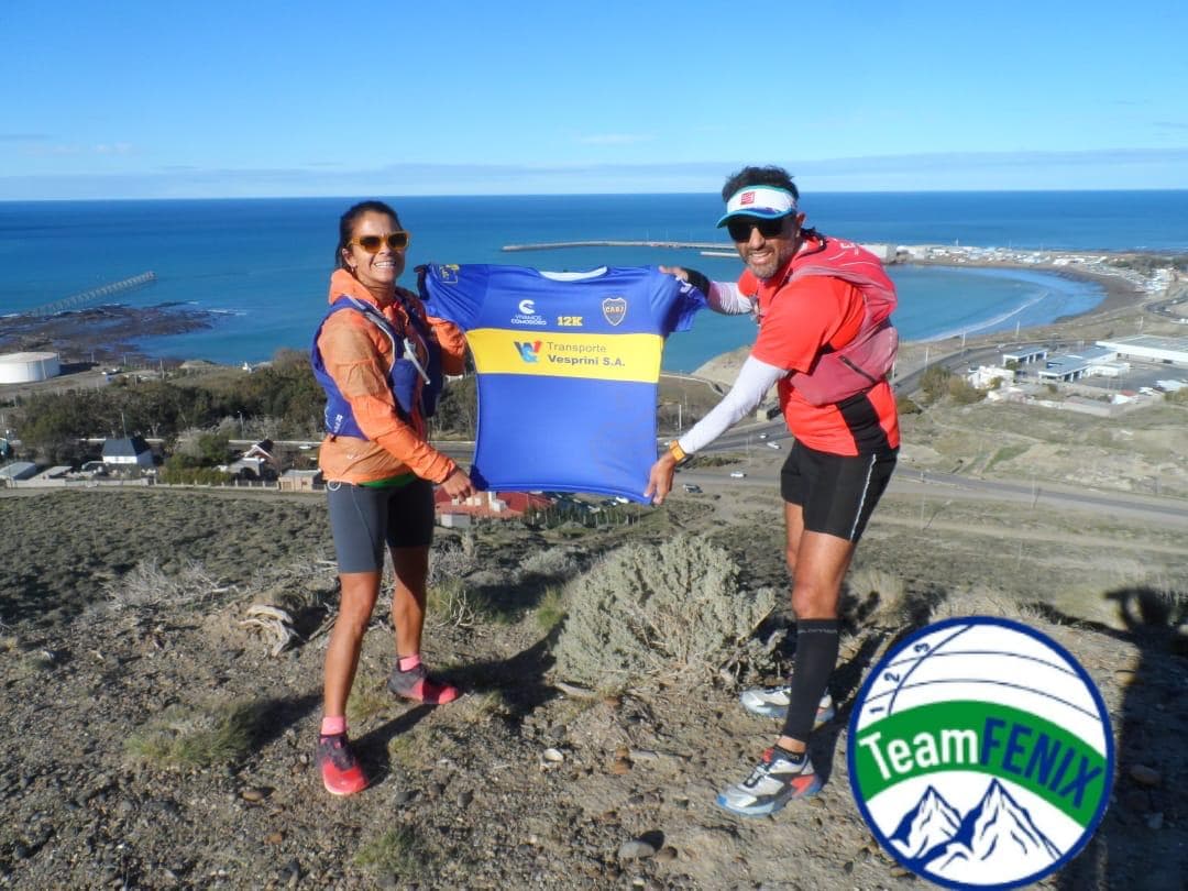Dos corredores con la camiseta oficial en lo alto de un cerro con vista al mar