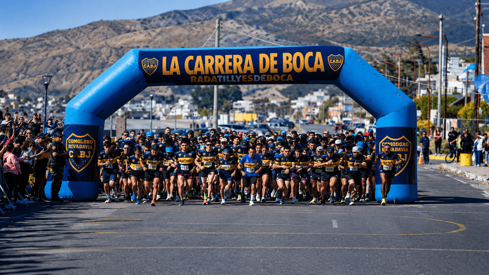 Largada de La Carrera de Boca bajo el arco, con el cordón montañoso patagónico de fondo